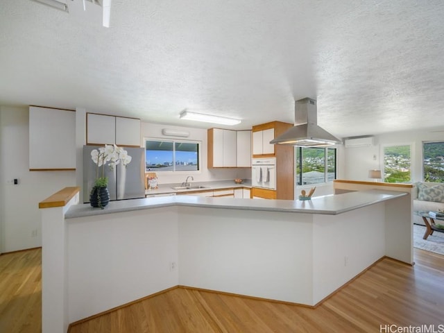 kitchen featuring a sink, oven, stainless steel fridge, light wood-type flooring, and island range hood