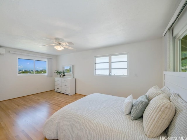 bedroom featuring a wall unit AC, ceiling fan, and light wood finished floors