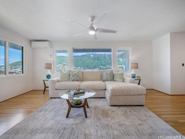 living area featuring a ceiling fan, a healthy amount of sunlight, wood finished floors, and a wall mounted AC