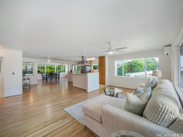 living room with a wealth of natural light, light wood-style floors, an AC wall unit, and ceiling fan