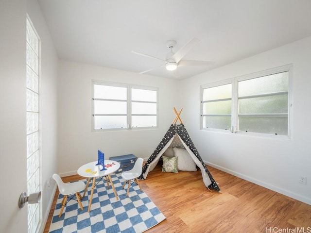 recreation room with a healthy amount of sunlight, a ceiling fan, baseboards, and wood finished floors