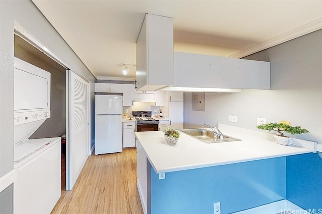 kitchen featuring stacked washer and clothes dryer, a sink, freestanding refrigerator, a peninsula, and gas range