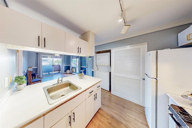 kitchen with light wood-style flooring, a sink, freestanding refrigerator, stacked washer / drying machine, and light countertops