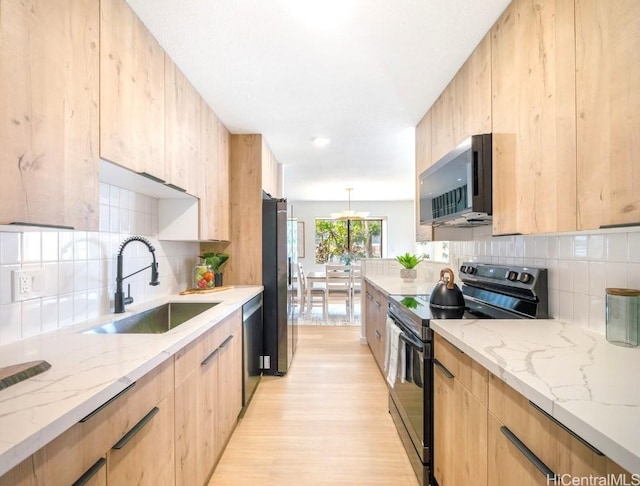 kitchen with light stone countertops, light brown cabinets, a sink, appliances with stainless steel finishes, and modern cabinets