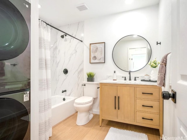 full bath with vanity, wood finished floors, visible vents, stacked washer and clothes dryer, and toilet