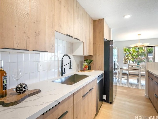 kitchen with a sink, light stone countertops, light brown cabinetry, stainless steel appliances, and modern cabinets