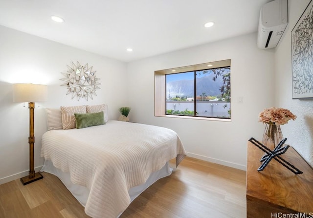 bedroom with an AC wall unit, recessed lighting, wood finished floors, and baseboards