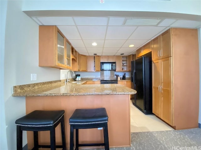 kitchen featuring visible vents, black appliances, a sink, a peninsula, and light stone countertops