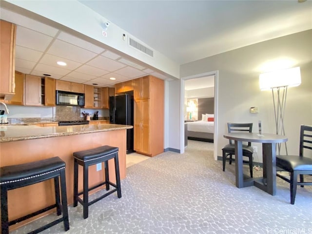 kitchen featuring visible vents, a peninsula, a sink, black appliances, and light carpet