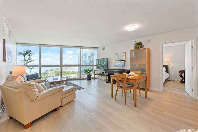 living area featuring visible vents, baseboards, a wall of windows, and light wood-style floors