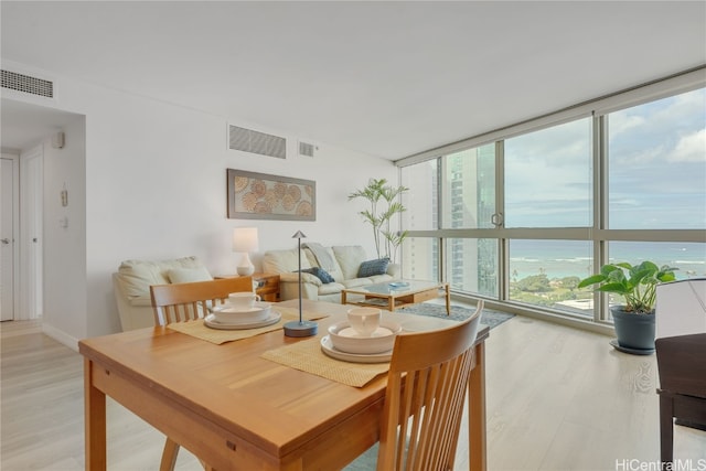 dining space with light wood finished floors, visible vents, and a wall of windows