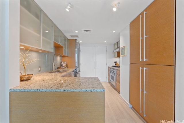 kitchen with a sink, light stone counters, a peninsula, white oven, and glass insert cabinets