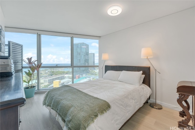 bedroom with a wall of windows, baseboards, a city view, and wood finished floors