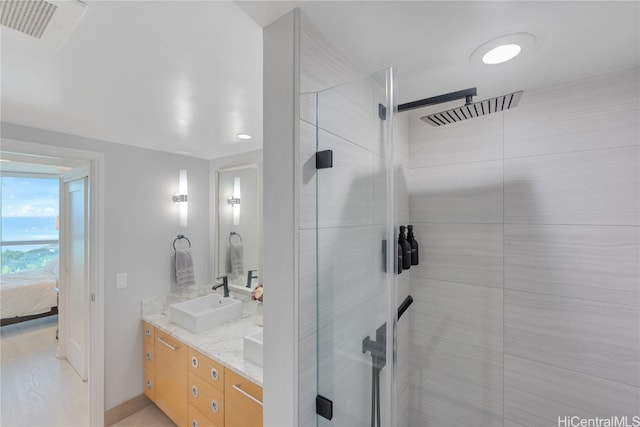 ensuite bathroom featuring visible vents, connected bathroom, double vanity, a tile shower, and a sink