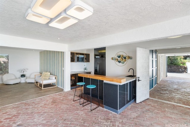 kitchen featuring brick floor, a breakfast bar, butcher block counters, and black fridge