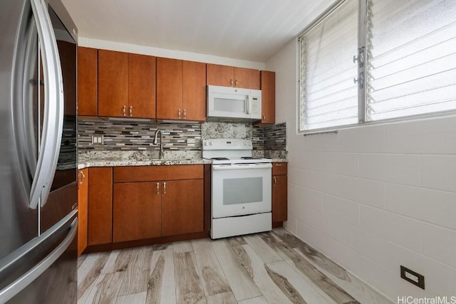 kitchen with white appliances, brown cabinetry, light wood-type flooring, and a sink