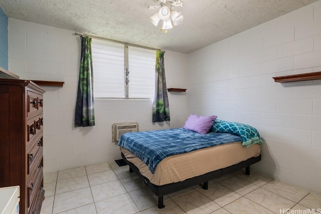 bedroom with a textured ceiling, concrete block wall, light tile patterned floors, and a wall mounted AC