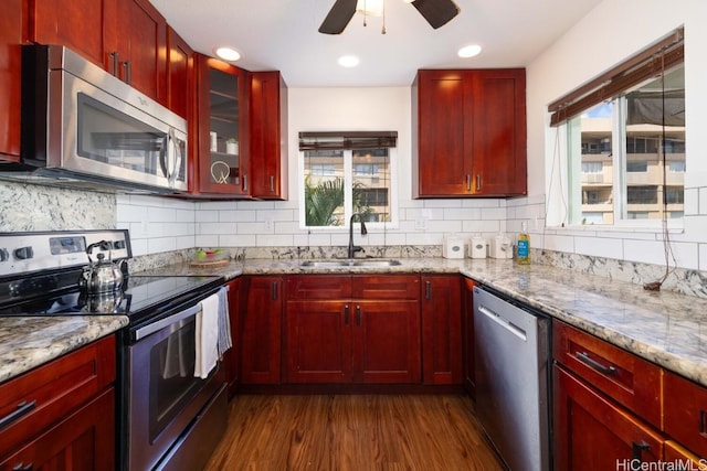 kitchen with a sink, backsplash, light stone countertops, appliances with stainless steel finishes, and reddish brown cabinets