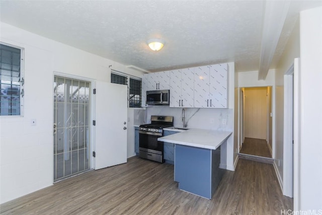 kitchen featuring a textured ceiling, dark wood-style floors, stainless steel appliances, a peninsula, and light countertops