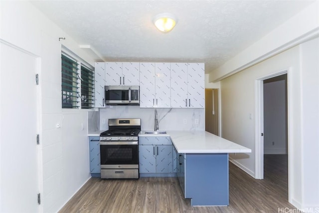 kitchen featuring a sink, a textured ceiling, dark wood finished floors, appliances with stainless steel finishes, and a peninsula