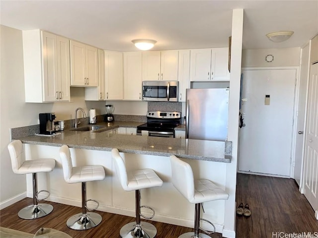 kitchen with a sink, appliances with stainless steel finishes, a peninsula, white cabinets, and dark wood-style flooring