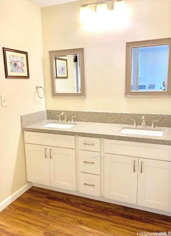 full bathroom featuring double vanity, wood finished floors, baseboards, and a sink