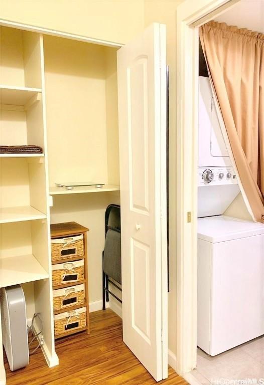 laundry area with stacked washer / drying machine, baseboards, light wood-style flooring, and laundry area