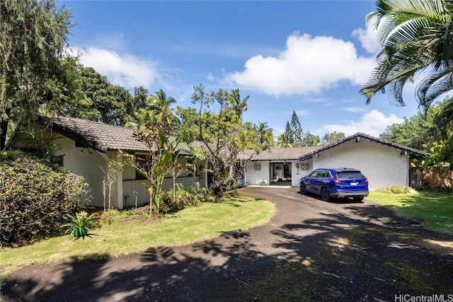 single story home featuring a tiled roof, aphalt driveway, a front lawn, and stucco siding