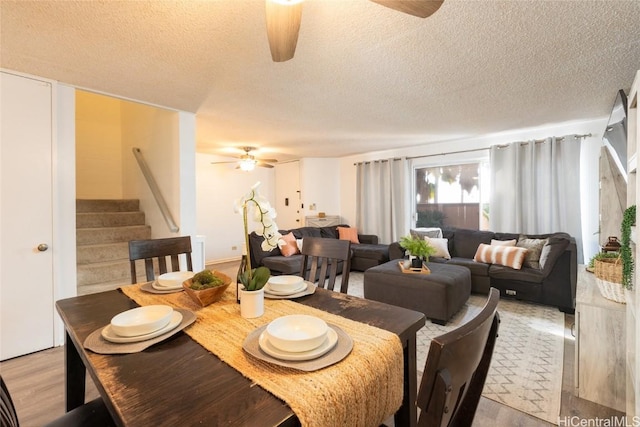 dining area with a textured ceiling, stairway, light wood-style floors, and ceiling fan