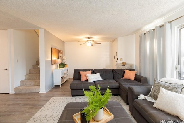 living area featuring ceiling fan, stairway, wood finished floors, and a textured ceiling