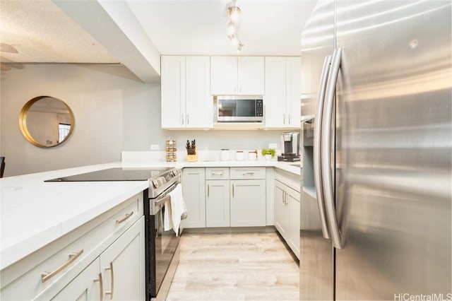 kitchen with stainless steel appliances, light countertops, track lighting, light wood-style floors, and white cabinetry