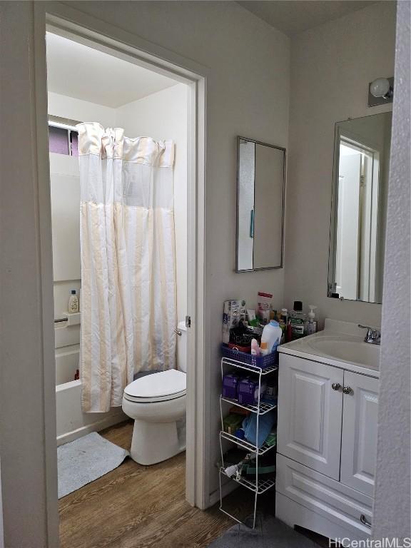 bathroom featuring vanity, shower / bathtub combination with curtain, toilet, and wood finished floors