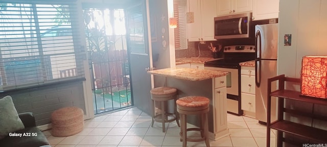 423 Kaiolu St Unit 106, Honolulu, HI 96815 - kitchen with appliances with stainless steel finishes, light tile patterned flooring, white cabinetry, light stone counters, and a kitchen bar