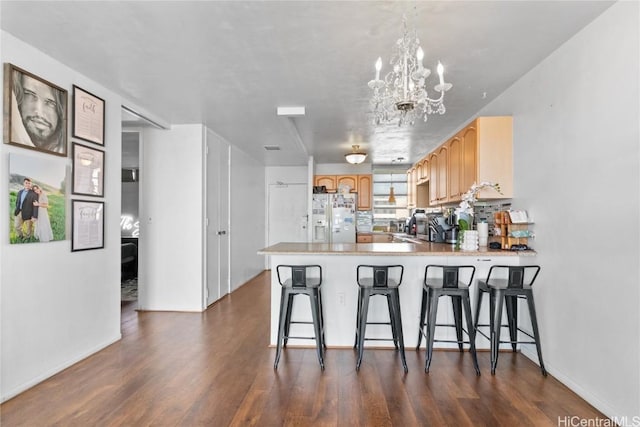 kitchen with dark wood-style floors, a peninsula, light countertops, white refrigerator with ice dispenser, and a kitchen bar