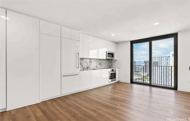 kitchen featuring wood finished floors, a sink, stainless steel appliances, white cabinetry, and modern cabinets