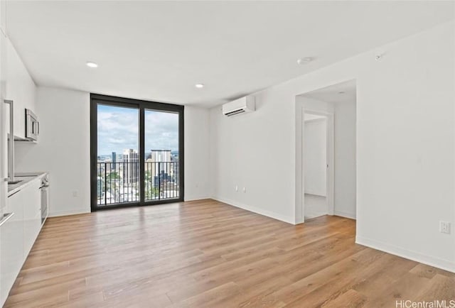 unfurnished room with a wall of windows, baseboards, light wood-style flooring, and a wall mounted AC