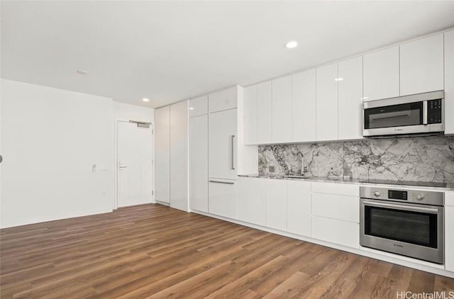 kitchen with stainless steel appliances, backsplash, dark wood-style floors, and white cabinets