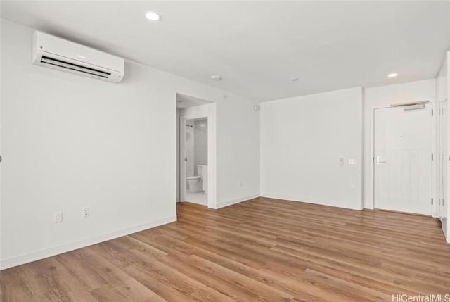 unfurnished room featuring recessed lighting, a wall mounted air conditioner, light wood-type flooring, and baseboards