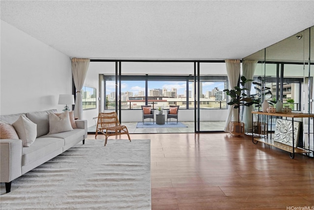 living area with expansive windows, a view of city, a textured ceiling, and wood finished floors