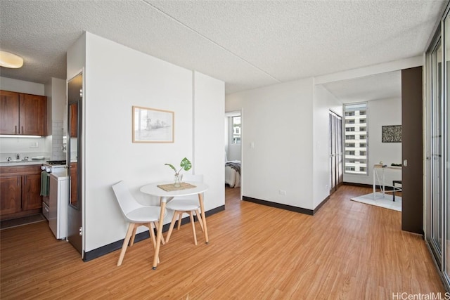 dining room featuring baseboards, light wood-style floors, and a textured ceiling