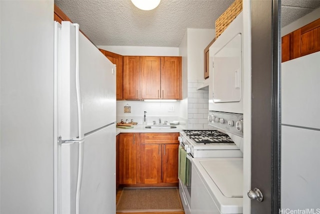 kitchen with brown cabinets, white appliances, light countertops, and stacked washer and dryer