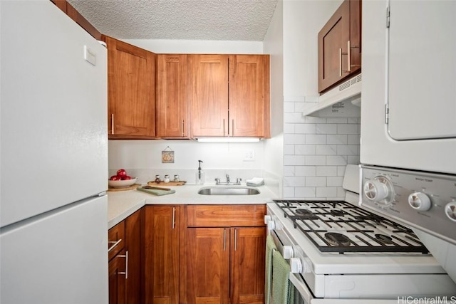 kitchen with a sink, under cabinet range hood, a textured ceiling, white appliances, and light countertops