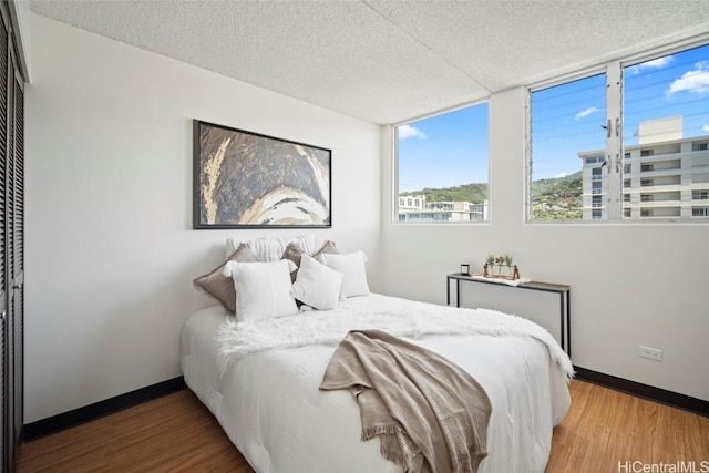 bedroom with baseboards, a textured ceiling, and wood finished floors