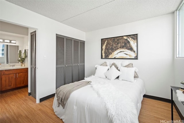 bedroom featuring light wood-type flooring, ensuite bathroom, a sink, a textured ceiling, and baseboards