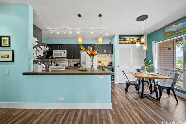 kitchen featuring decorative light fixtures, dark countertops, white appliances, a peninsula, and dark wood-style flooring