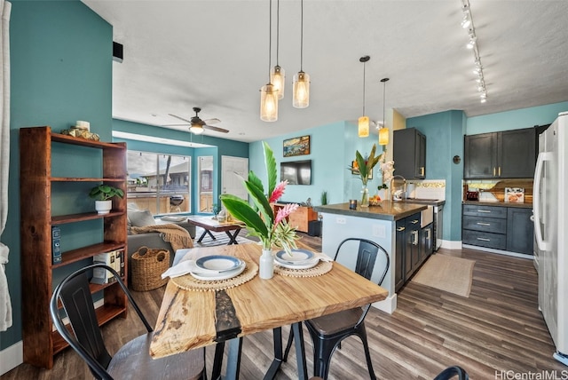 dining room with dark wood finished floors, rail lighting, baseboards, and ceiling fan