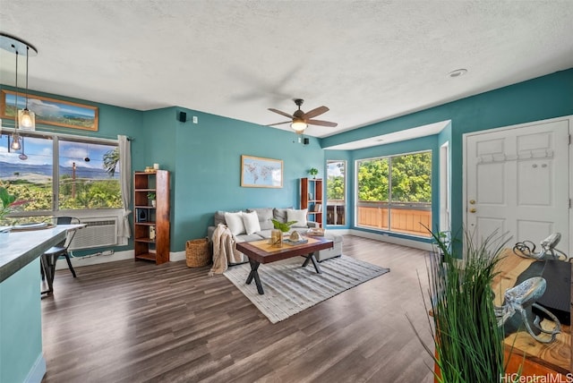 living area featuring a baseboard heating unit, baseboards, wood finished floors, a textured ceiling, and a ceiling fan