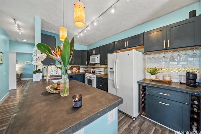 kitchen with track lighting, backsplash, dark wood finished floors, pendant lighting, and white appliances