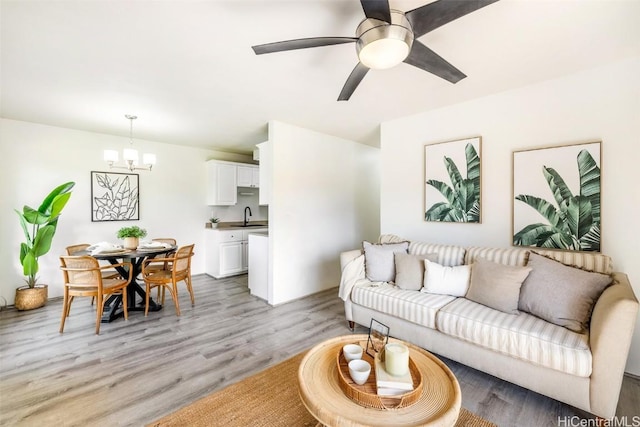 living room with light wood-type flooring and ceiling fan with notable chandelier