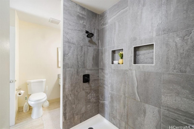 full bath with visible vents, baseboards, toilet, and a tile shower